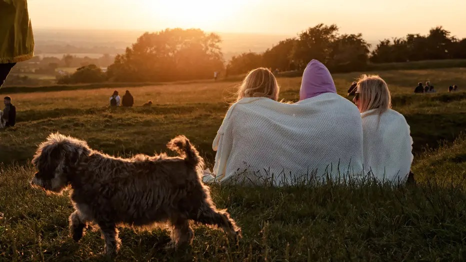 FILE IMAGE - Three women sitting and watching the sunset while a small dog walks by. Hundreds of people gathered in the Hill of Tara for the Summer Solstice of 2021. (Photo by Natalia Campos/SOPA Images/LightRocket via Getty Images)